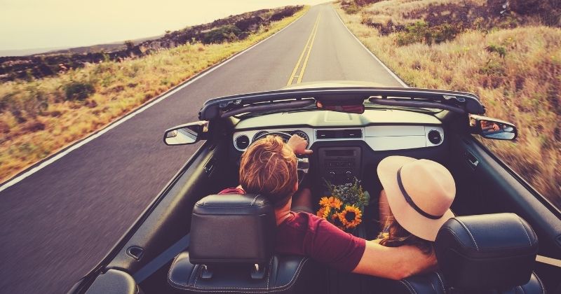 Conducteur et passagère dans une voiture cabriolet, sur une route ensoleillée.