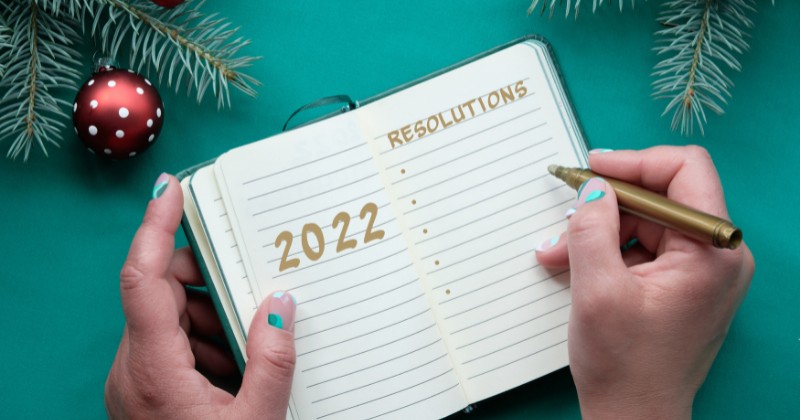 Mains écrivant sur un calepin les bonnes résolutions pour l'année 2022
