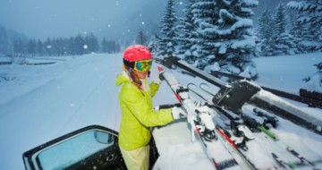 Femme habillée pour skier installant des skis sur le toit d'une voiture sur route enneigée