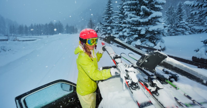 Femme habillée pour skier installant des skis sur le toit d'une voiture sur route enneigée