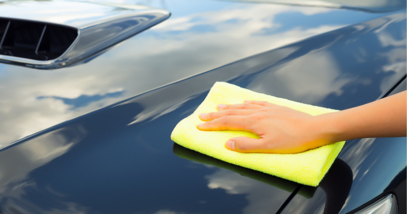 Main de femme lustrant la carrosserie d'une voiture avec un tissu