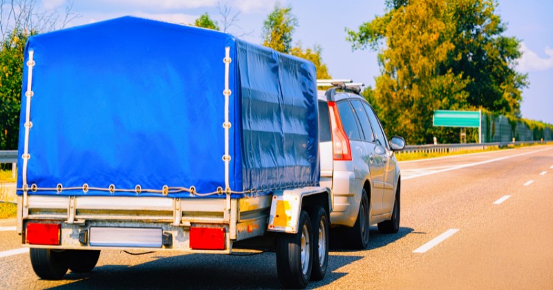 Voiture roulant sur autoroute avec une remorque couverte à l'arrière.