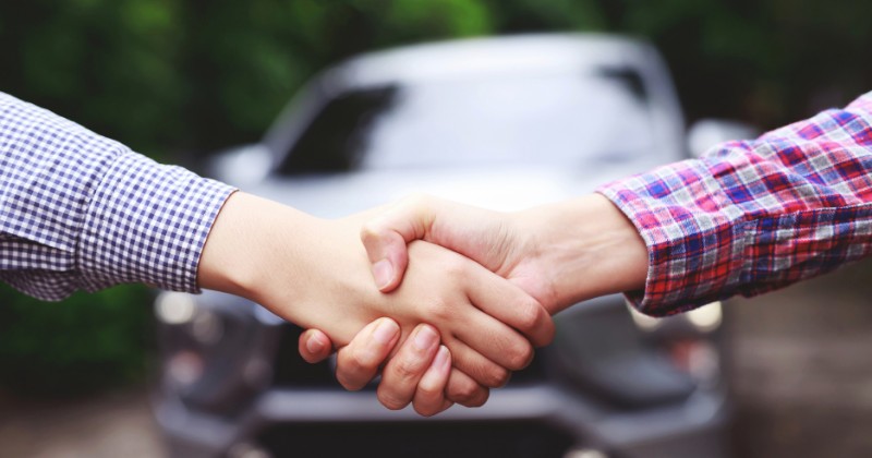 Poignée de mains devant une voiture pour symboliser un contrat de vente ou de location